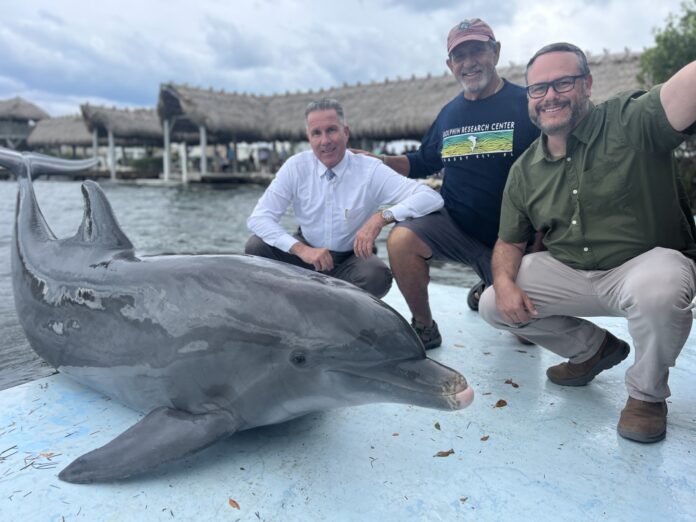 three men pose with a dolphin statue on a boat