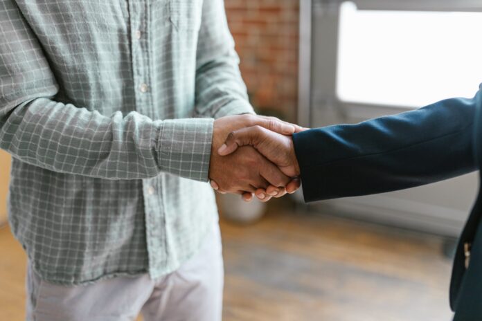 pexels-photo-7414003 two men shaking hands in front of a window