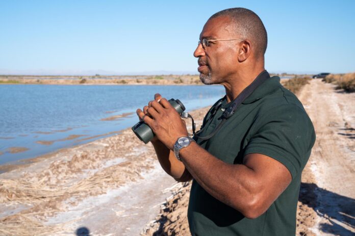 a man standing on a dirt road next to a body of water