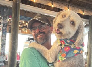 a man holding a dog wearing a bandana