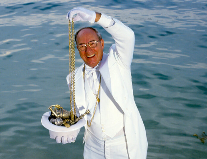 a man in a white suit and tie holding a chain