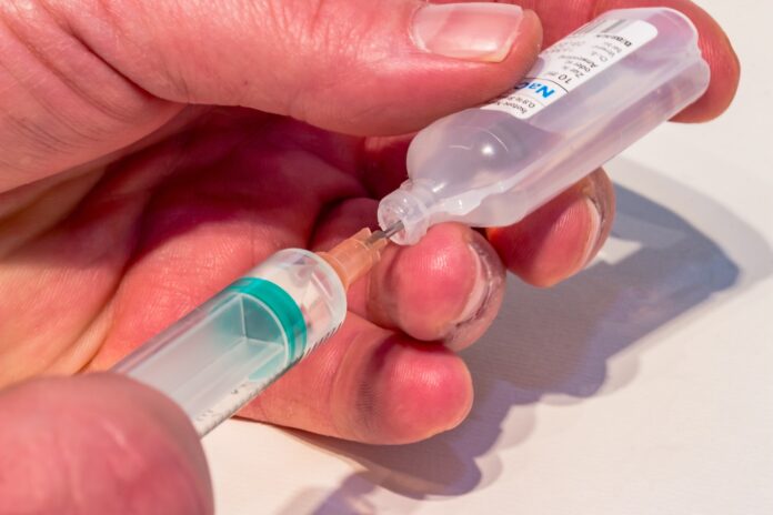 a hand holding a small plastic bottle with a needle in it