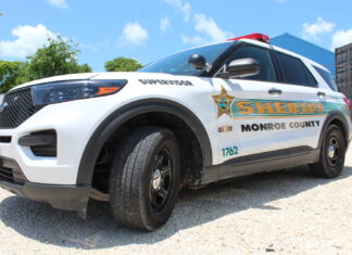 ARREST WARRANT LEADS TO DISCOVERY OF STOLEN CREDIT CARDS & DRUGS INSIDE A KEY LARGO MOTEL ROOM a white police car parked in a parking lot