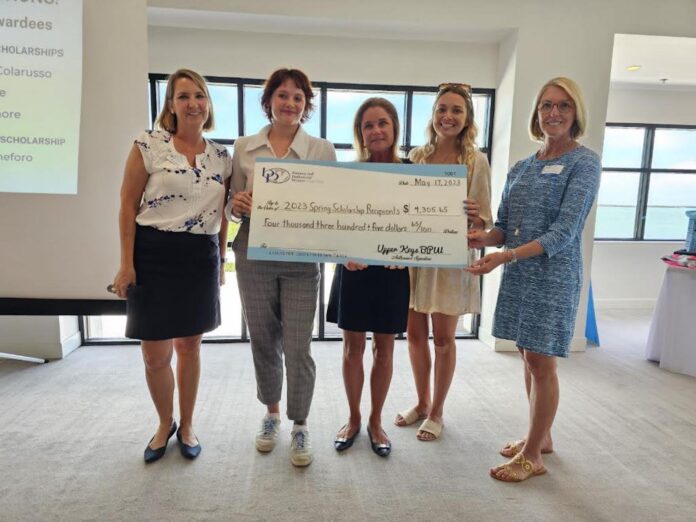 a group of women standing next to each other holding a check