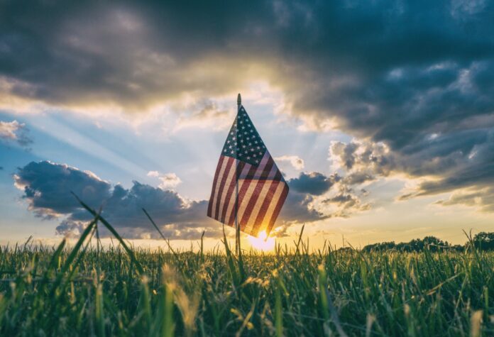 a flag in the grass with the sun behind it