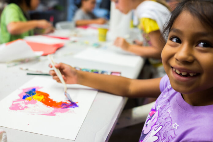 a little girl is smiling while painting on a canvas
