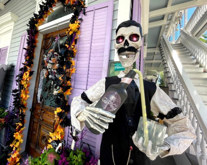 a skeleton holding a bottle in front of a house