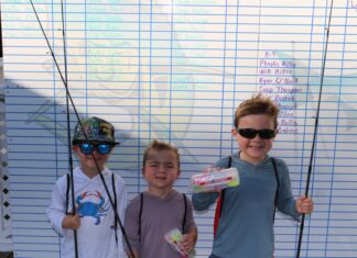 three young boys holding fishing rods in front of a sign