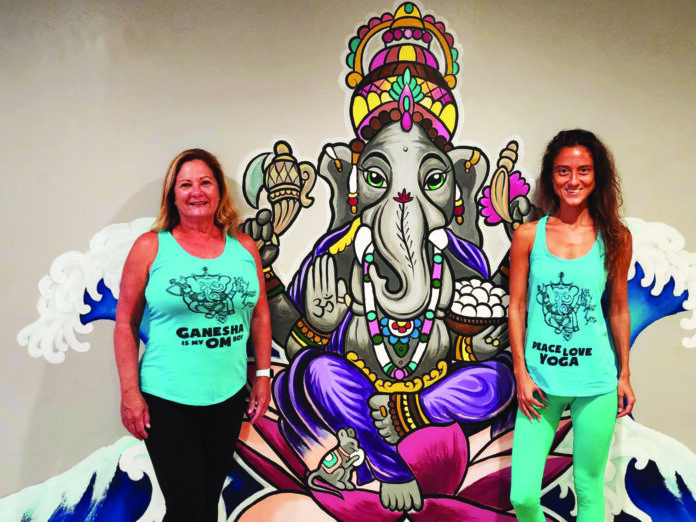 two women standing in front of a painting of a ganeshi