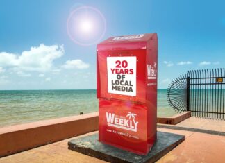 a red box sitting on top of a sidewalk next to the ocean