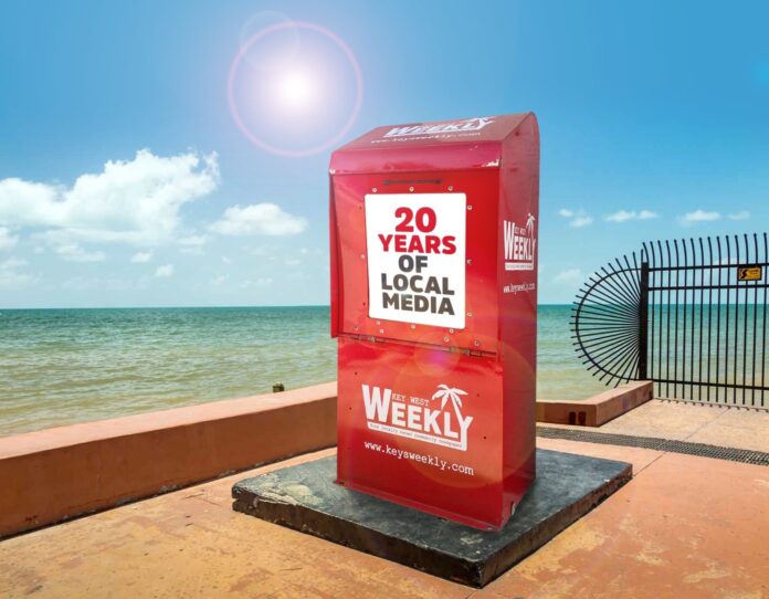 a red box sitting on top of a sidewalk next to the ocean