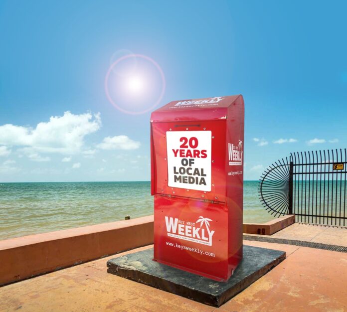 a red box sitting on top of a sidewalk near the ocean