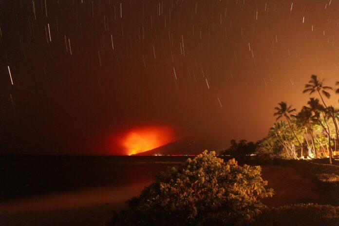 a night time view of a beach with palm trees and a volcano in the distance