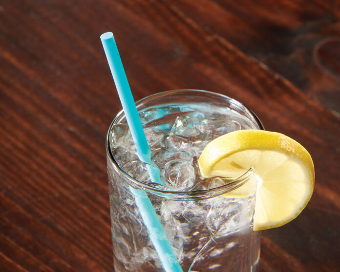 a glass with a blue straw and a lemon on a wooden table