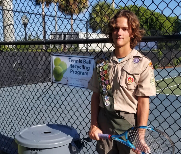 a young man holding a tennis racquet next to a trash can