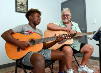 a man sitting next to another man holding a guitar
