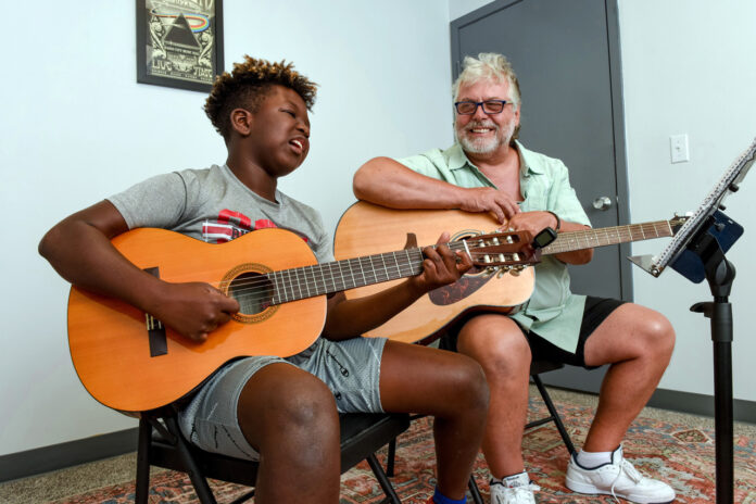 a man sitting next to another man holding a guitar