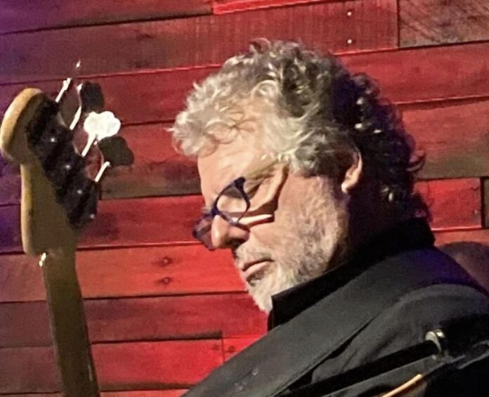 a man with curly hair and glasses holding a guitar