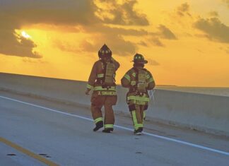 two fire fighters walking down a highway at sunset