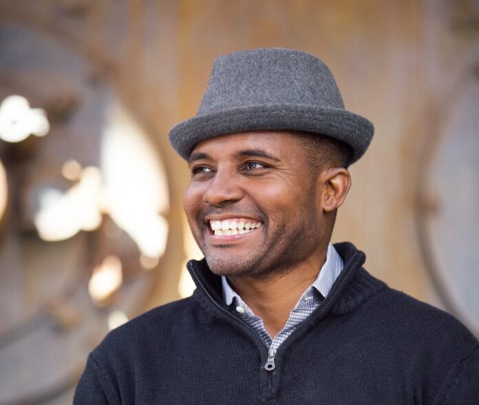 a man in a hat smiles while standing in front of barrels