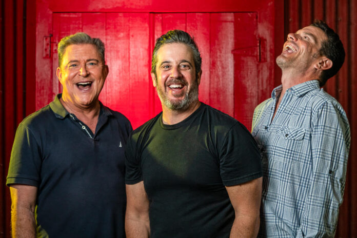 three men standing next to each other in front of a red door