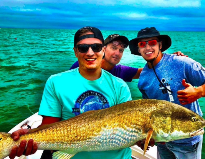 three men on a boat holding a large fish