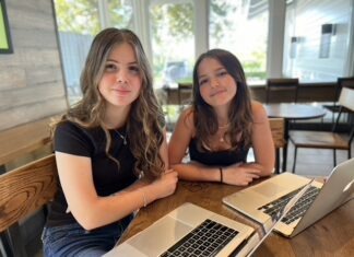 two girls sitting at a table with laptops