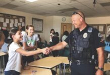 a police officer shaking hands with a girl in a classroom