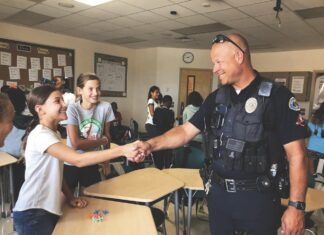 a police officer shaking hands with a girl in a classroom