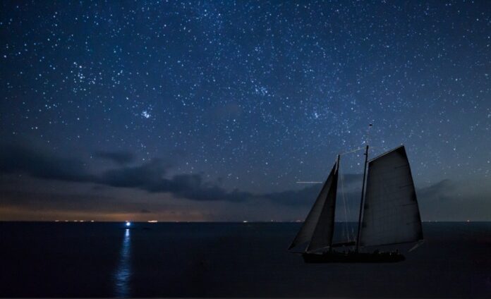 a sailboat in the ocean under a night sky with stars