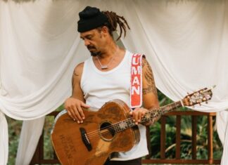 a man with dreadlocks playing a guitar under a canopy