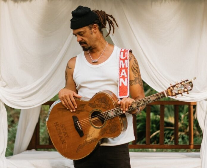 a man with dreadlocks playing a guitar under a canopy