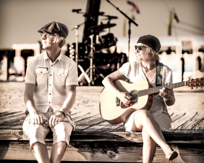a man and a woman sitting on a dock with a guitar