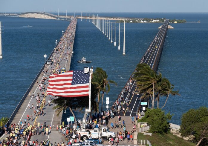 a crowd of people walking across a bridge next to the ocean