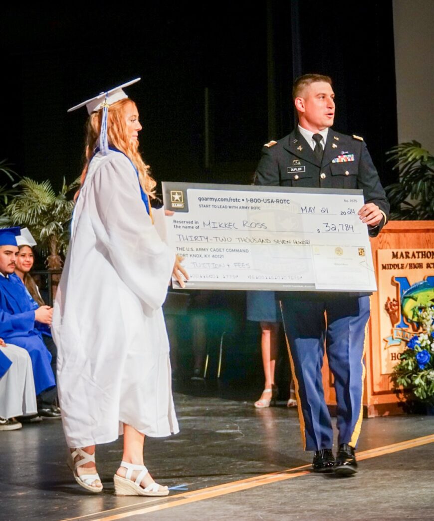 a woman in a graduation gown holding a large cheque