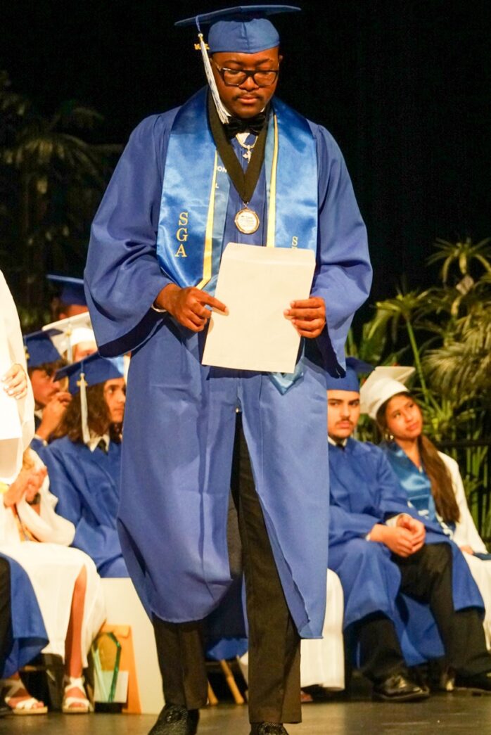 a man in a blue graduation gown holding a piece of paper