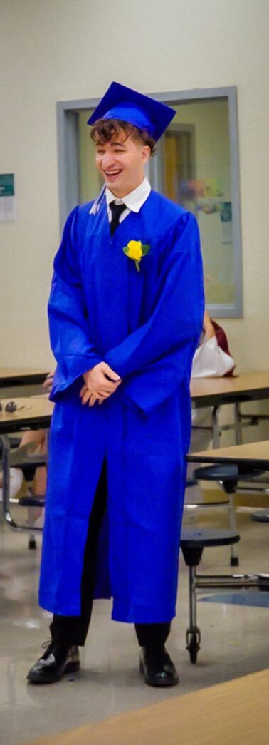 a man in a blue graduation gown standing in a classroom