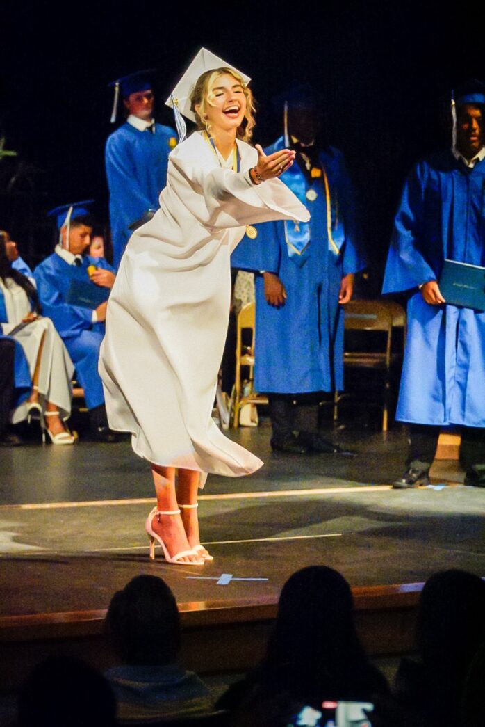 a woman in a graduation gown is dancing on stage