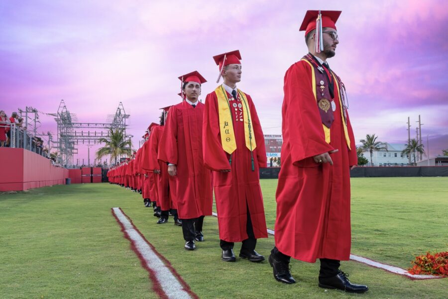 a group of men in red graduation gowns standing on a field