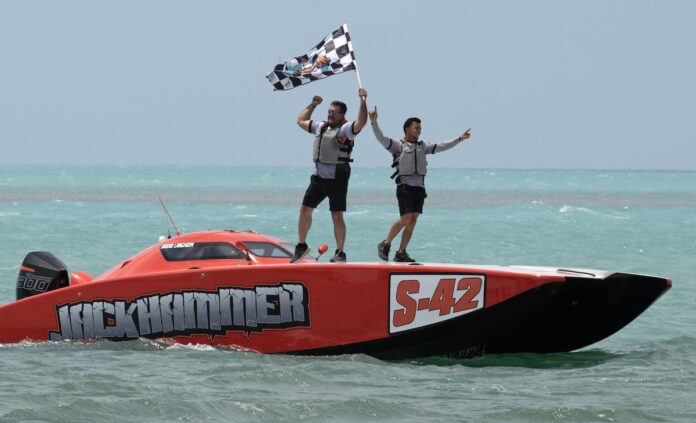 two men standing on top of a speed boat in the ocean