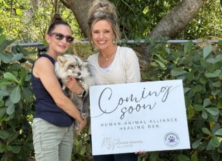 two women holding a small dog in front of a sign