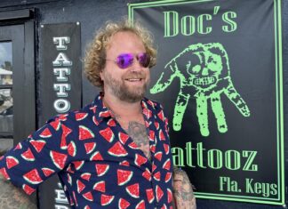 a man in a shirt and sunglasses standing in front of a tattoo shop