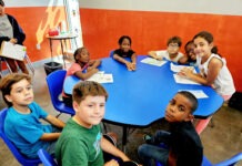 a group of children sitting around a blue table
