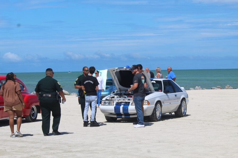 a group of people standing around a car on the beach
