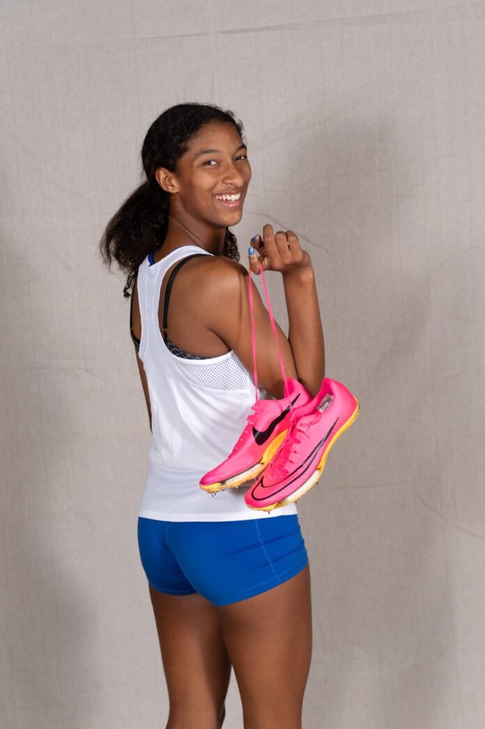 a woman in a white tank top and blue shorts holding a pink bag