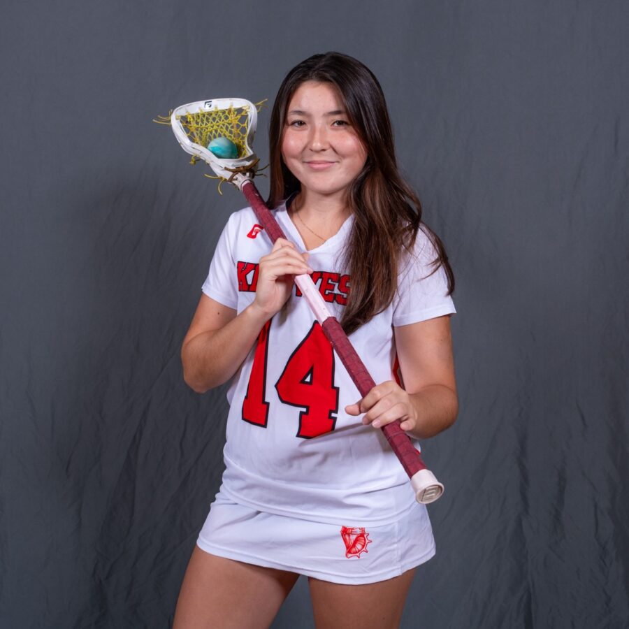 a girl in a white uniform holding a lacrosse stick
