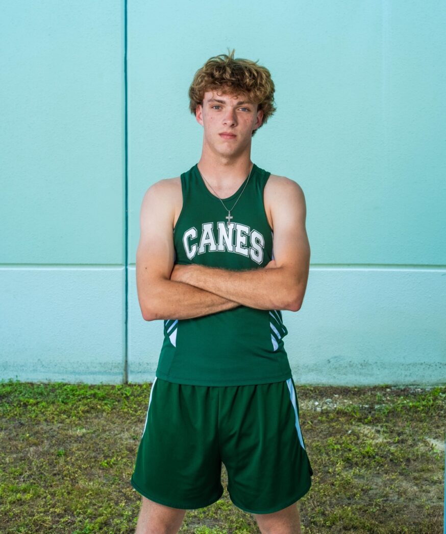 a young man in a green tank top standing in front of a blue wall