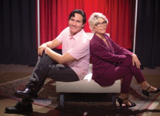 a man and a woman sitting on a couch in front of a red curtain