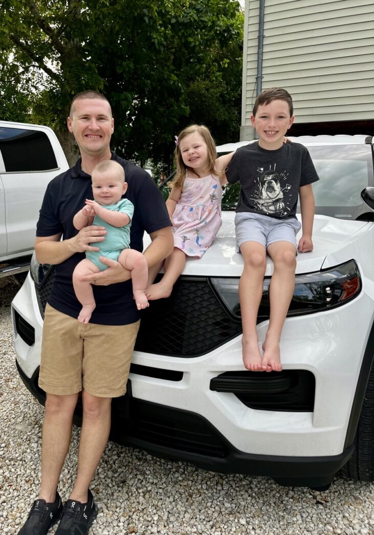 a man and two children sitting on the hood of a car