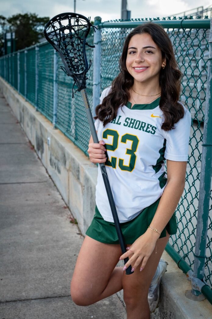 a woman in a green and white uniform holding a lacrosse stick